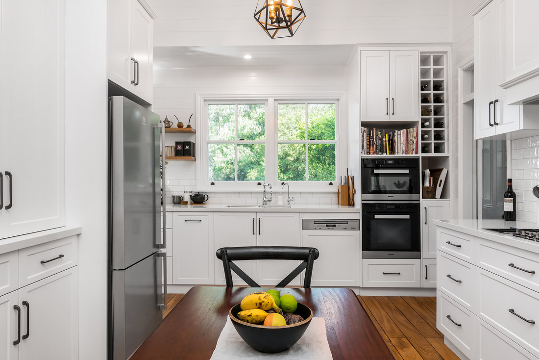 A white shaker kitchen with timber benchtop and a window over the sink