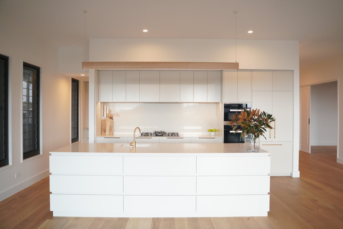 A white kitchen with a large island bench and timber floors